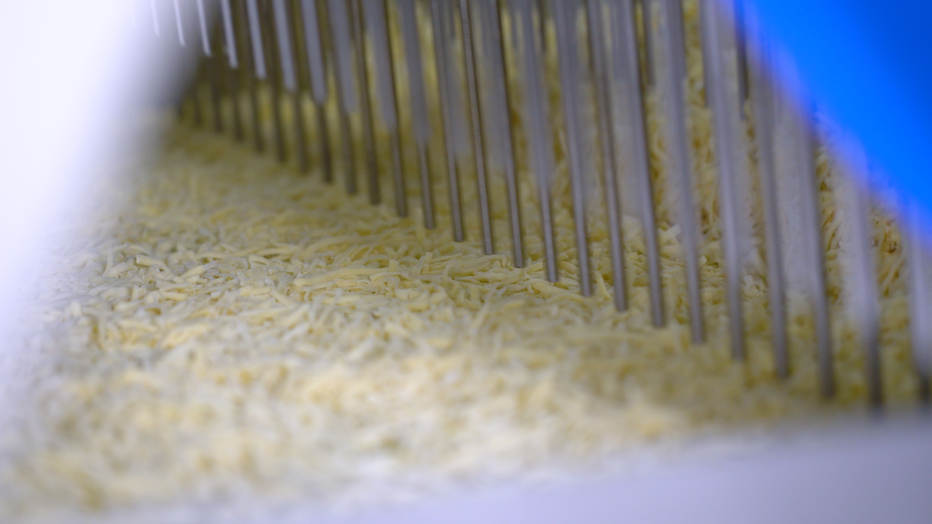 A close up of cheese moving through a pizza topping applicator. 